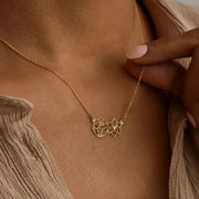 Woman model wearing 14k gold filled necklace with a cut-out birth flower pendant on a textured surface with leaves.